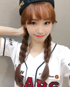 a girl with long hair wearing a baseball uniform and holding her hands behind her head