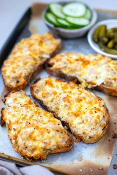 several pieces of bread with cheese and pickles on the side, along with two bowls of pickles