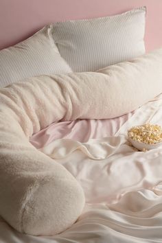 a large round pillow on top of a bed next to pillows and a bowl of popcorn