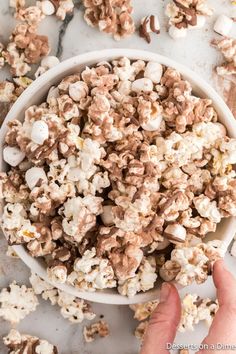 a bowl filled with chocolate popcorn sitting on top of a white counter next to a person's hand