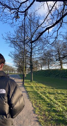 a man in a black jacket is walking down the street with his back turned to the camera