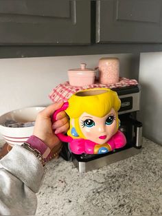 a person holding a toy in front of a toaster oven and counter top with dishes on it