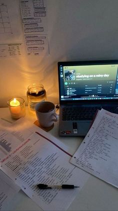 an open laptop computer sitting on top of a desk next to papers and a cup