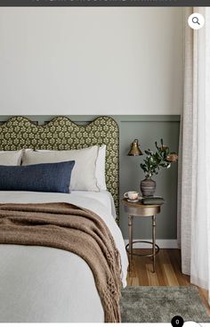 a white bed sitting next to a window with curtains on top of it and a small table in front of it