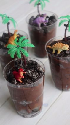 four plastic cups filled with chocolate pudding and small toy dinosaurs