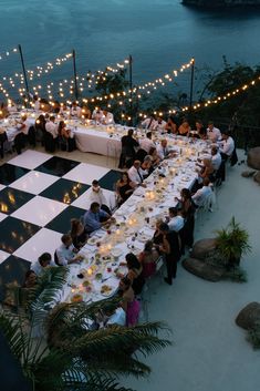 a large chess board is set up for a formal dinner by the water at dusk