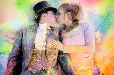 two people are kissing in front of colored powder on the ground and one person is wearing a top hat