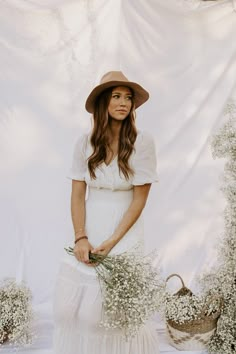 a woman in a white dress and hat holding flowers