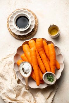 a plate with some carrots on it next to two cups and saucers filled with seasonings