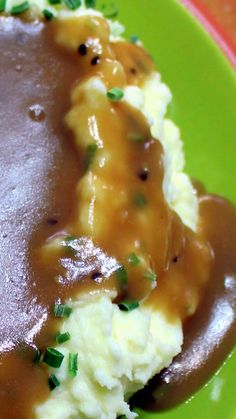 mashed potatoes covered in gravy on a green plate with garnish