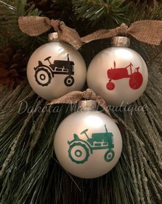 three christmas ornaments with tractors on them hanging from a pine tree in front of a pine cone