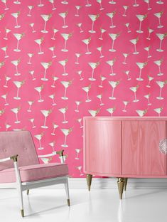 two chairs and a cabinet in front of a pink wall with martini glasses on it