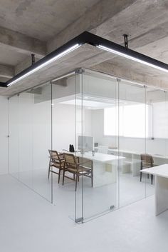 an empty office with glass walls and wooden chairs in the center, surrounded by white desks