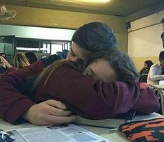 two people hugging each other while sitting at a table in front of a laptop computer