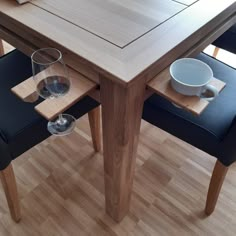 two empty wine glasses sitting on the edge of a wooden table with black leather chairs