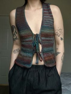 a woman with tattoos on her chest wearing a knitted vest