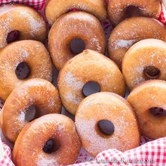 many donuts are covered with powdered sugar and cherries on a tablecloth