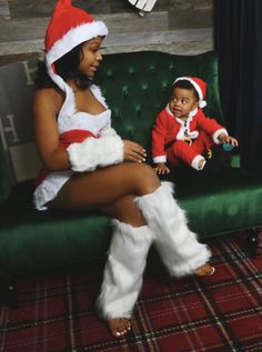 a woman sitting on top of a green couch next to a baby wearing santa clause clothes