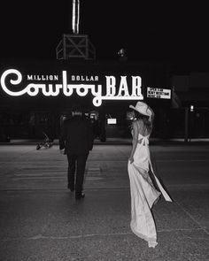 black and white photograph of a woman walking in front of a sign that reads,'million dollar cowboy bar '