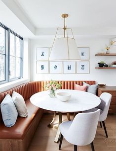 a dining room table with white chairs and a bench in front of the window that has pictures on it