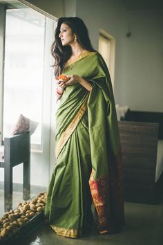 a woman in a green sari standing by a window with food on the table