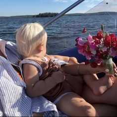 a woman holding a baby in her lap while sitting on a boat near the water