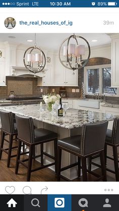 a kitchen with marble counter tops and white cabinets, two chandeliers hanging from the ceiling