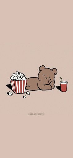 a brown teddy bear laying on the ground next to a cup of popcorn