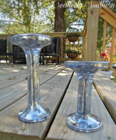 two clear wine glasses sitting on top of a wooden picnic table next to each other