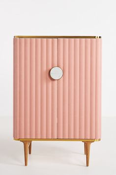 a pink cabinet with a mirror on the front and legs, against a white background