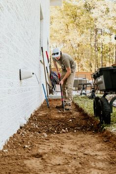 a man digging dirt in front of a white building with a black cat next to it