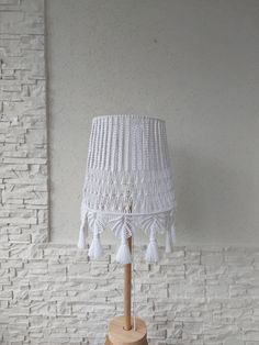 a white lamp with tassels on a wooden base in front of a brick wall