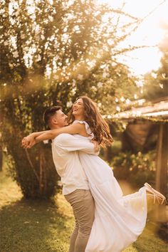 a man holding a woman in his arms while she holds her back and smiles at the camera