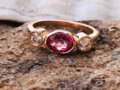 This beautiful three stone ring contains a .75ct lab created pink sapphire, with .20ct total moissanite on the sides. The ring is available in sterling silver, and 14k white, yellow or rose gold. This ring is available in a high polish or satin finish and can be completely customized with any color center and side stones. Please send me a message if you need a size not listed. All items are handmade by me in my shop in Woodbridge, NJ. Please message me with any questions. Shipping within the Uni Raw Tourmaline Ring, Teen Ring, Raw Pink Tourmaline, Stacked Engagement Ring, Morganite Earrings, Gemstone Stacking Ring, Pink Sapphire Ring Engagement, Raw Crystal Ring, Trio Ring