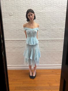 a woman standing in front of a white wall wearing a blue dress and black heels