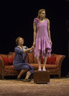 a woman in a pink dress standing next to a man sitting on a couch