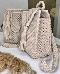 two crocheted handbags sitting on top of a table next to a feather