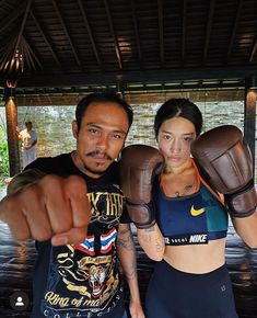 a man and woman standing next to each other with boxing gloves on their shoulders, pointing at the camera