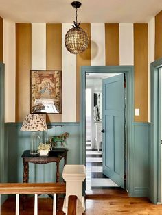 an entryway with striped walls and wooden flooring, blue front door leading to the hallway