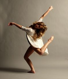 a young woman is dancing in the air with her arms out and legs spread wide