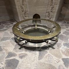 a round glass table with metal legs on stone flooring next to a brick wall