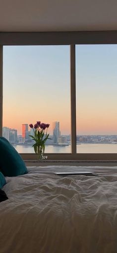 a bed sitting in front of two large windows next to a vase with flowers on it