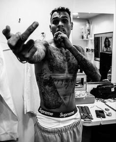 a man with tattoos on his chest and hands in the air, making a peace sign