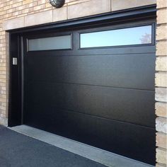 a black garage door on the side of a brick building with a clock above it