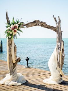 an arch made out of driftwood is decorated with flowers and greenery on the beach