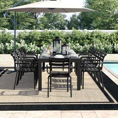 an outdoor dining table with umbrella over it next to a swimming pool in the background