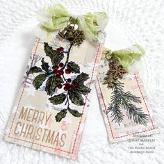 two tags decorated with holly and pine cones on a white background, one has a green bow