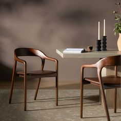 two wooden chairs sitting at a table with a vase and candles on top of it