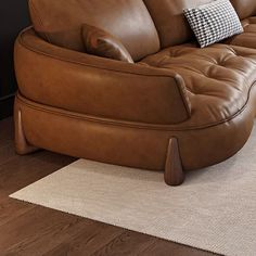 a brown leather couch sitting on top of a wooden floor next to a white rug