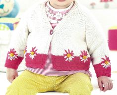 a baby sitting on the floor wearing a sweater and pants with flowers on it's sleeves